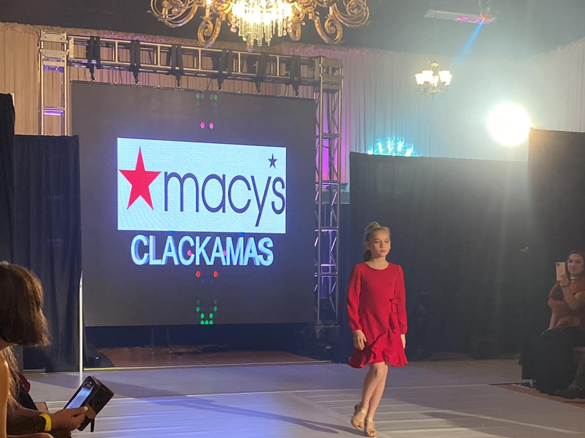 A young woman in a beautiful evening gown sings powerfully with her eyes closed. An image of raindrops on a window with blurred lights fill a large display behind her.